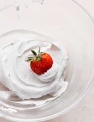 A red strawberry dipped into a pile of Coconut Whipped Cream.