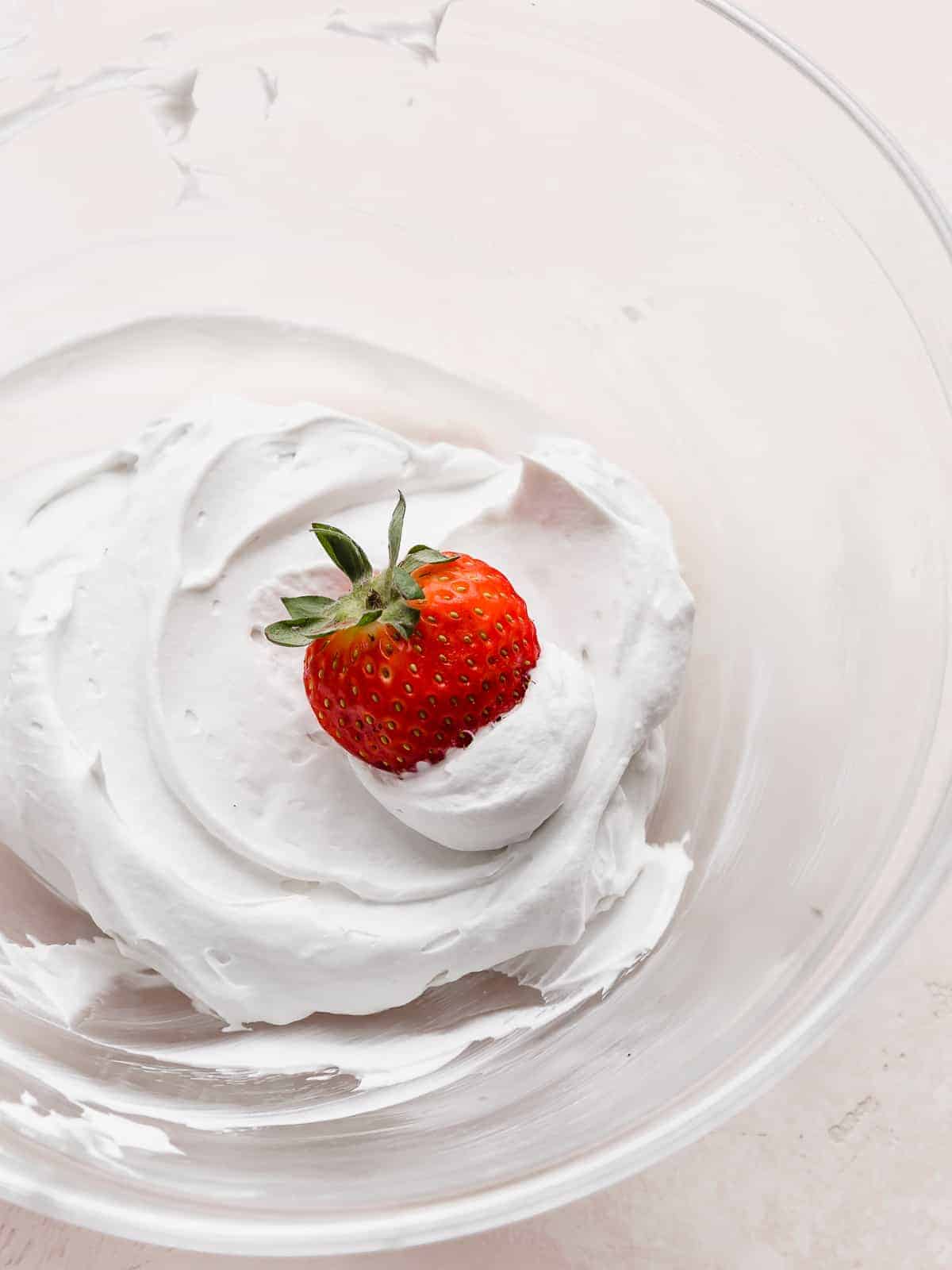 A red strawberry dipped into a pile of Coconut Whipped Cream.