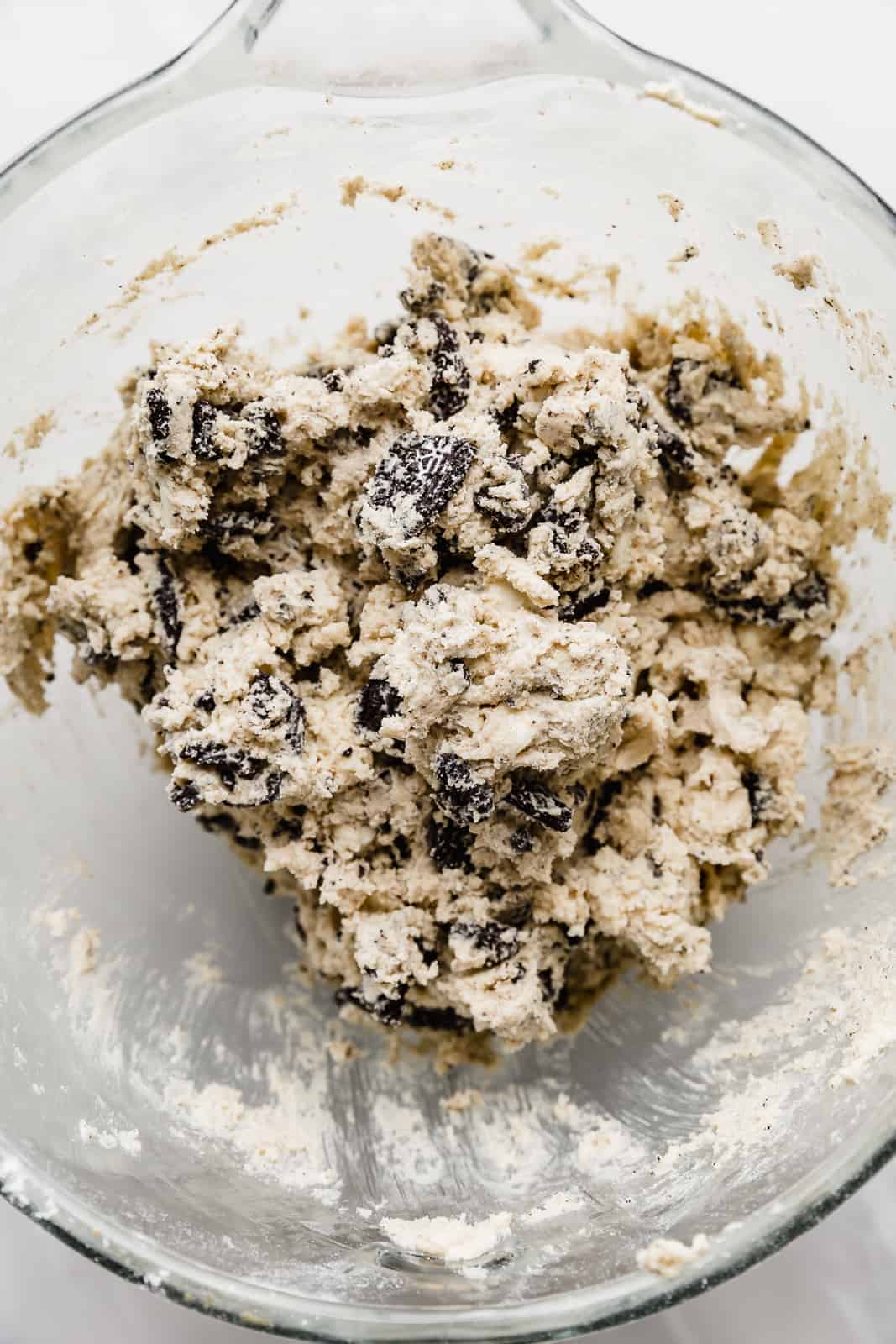 Cookies and Cream Cookie dough batter in a glass bowl against a white background.