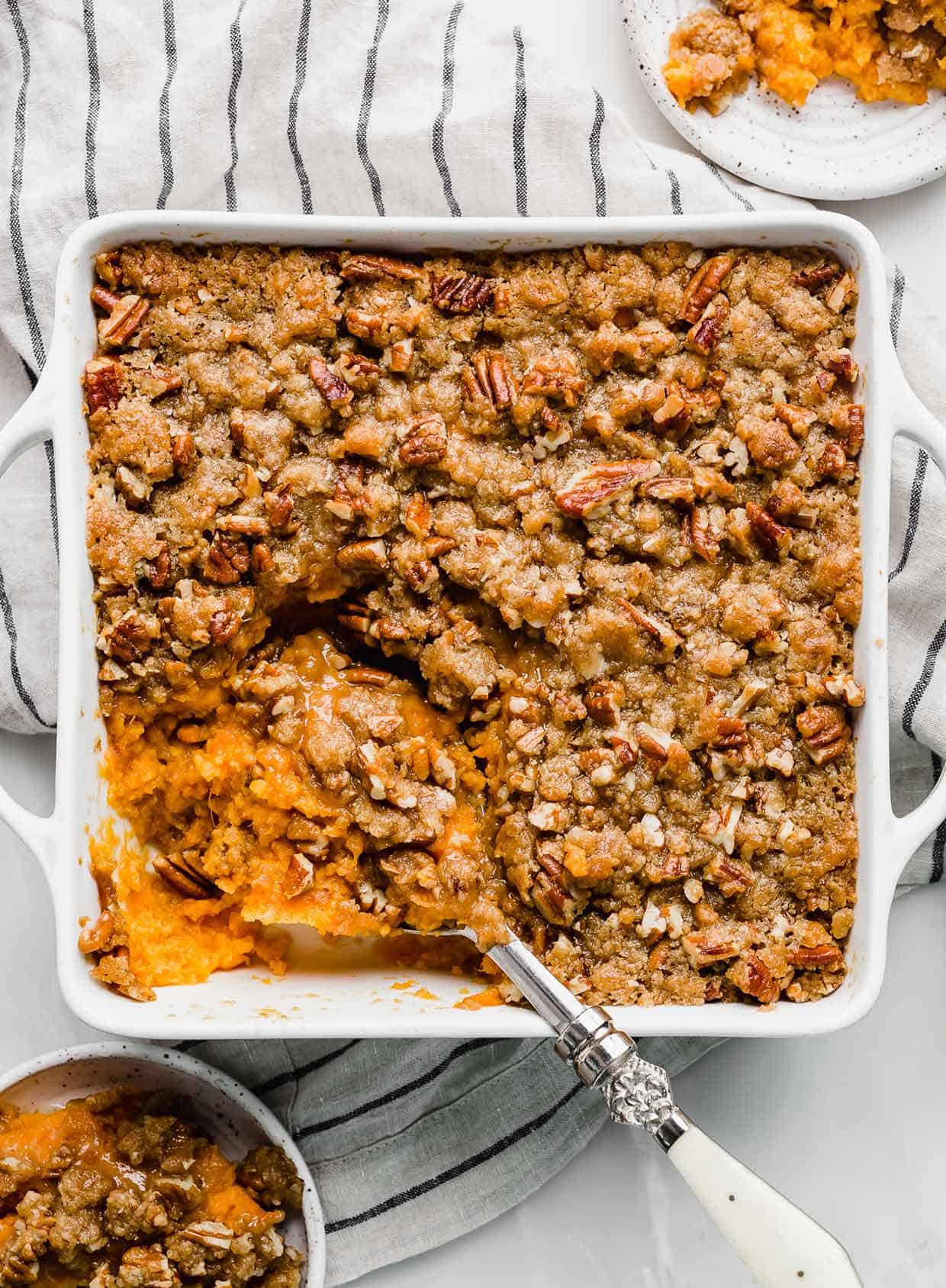 A serving spoon scooping out Easy Sweet Potato Casserole from a white square baking dish.