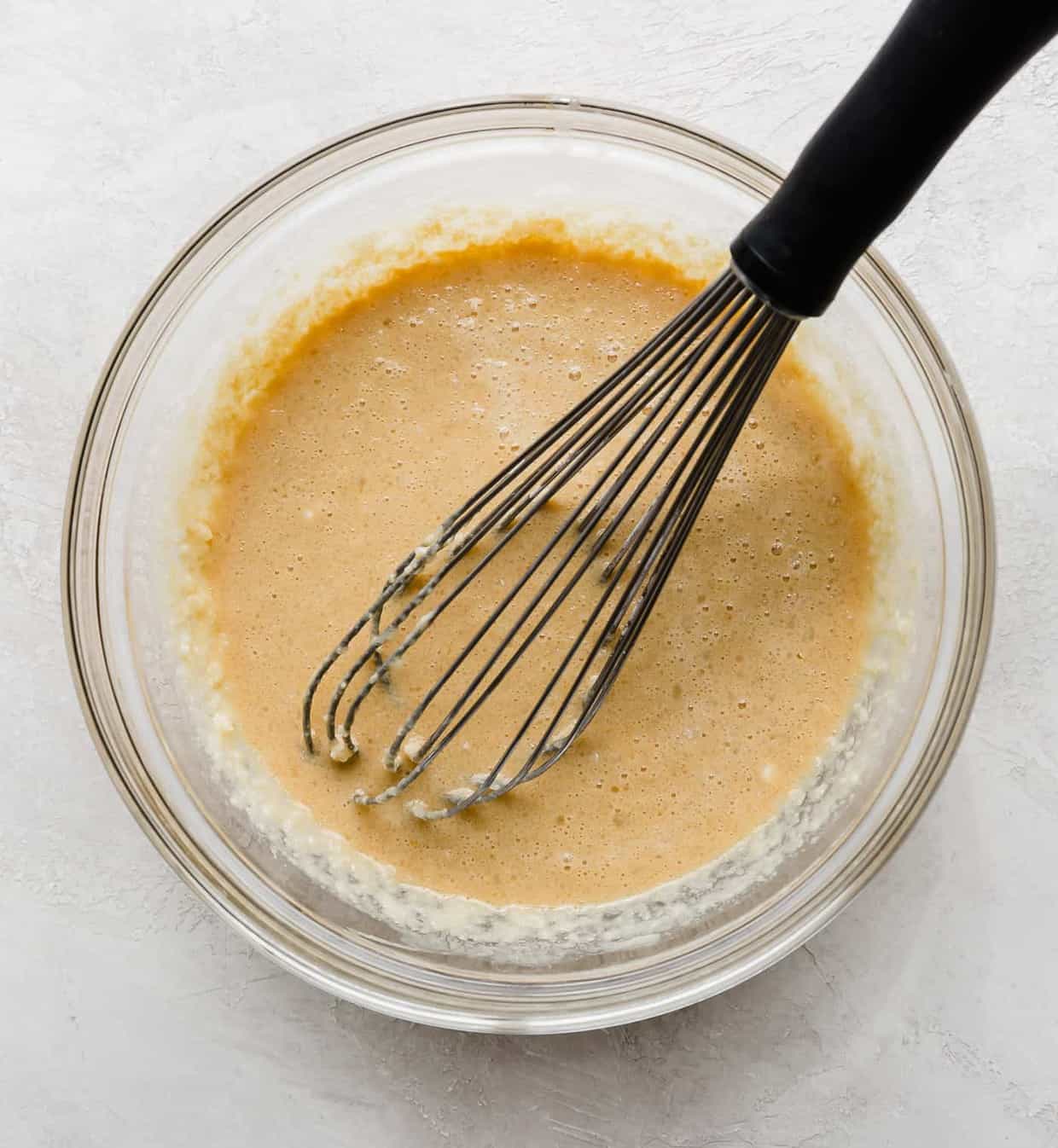 A whisk in a bowl of wet ingredients used to make waffles.
