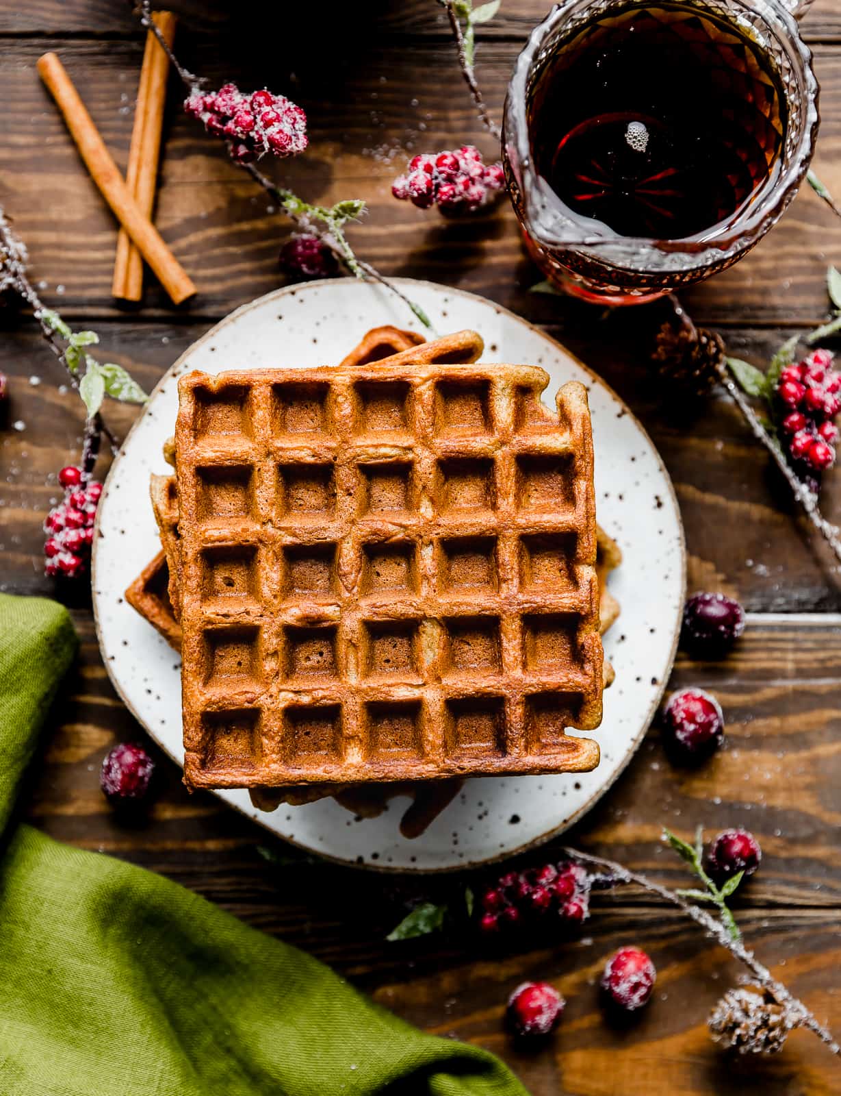 Square gingerbread waffles on a white plate with a green towel to the side.