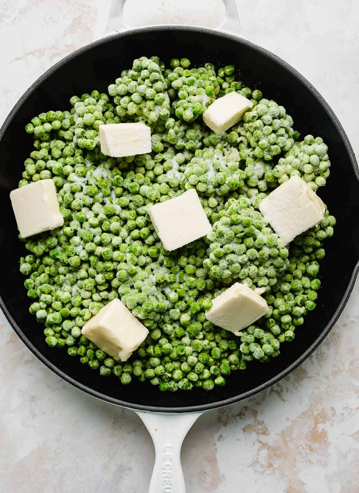 Frozen peas in a skillet with butter cubes scattered on top.