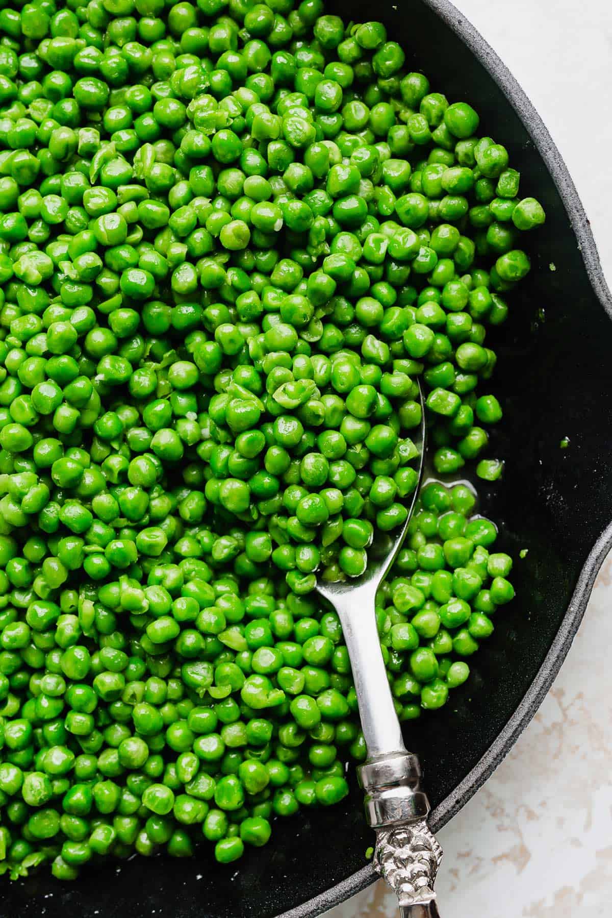 Cooked peas in a skillet with a serving spoon scooping some out.