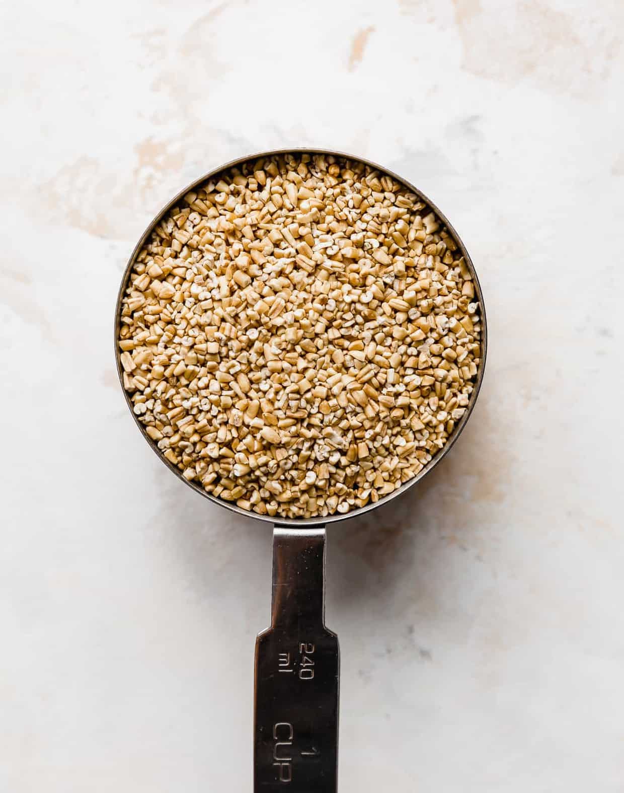 A metal measuring cup full of raw steel cut oats.