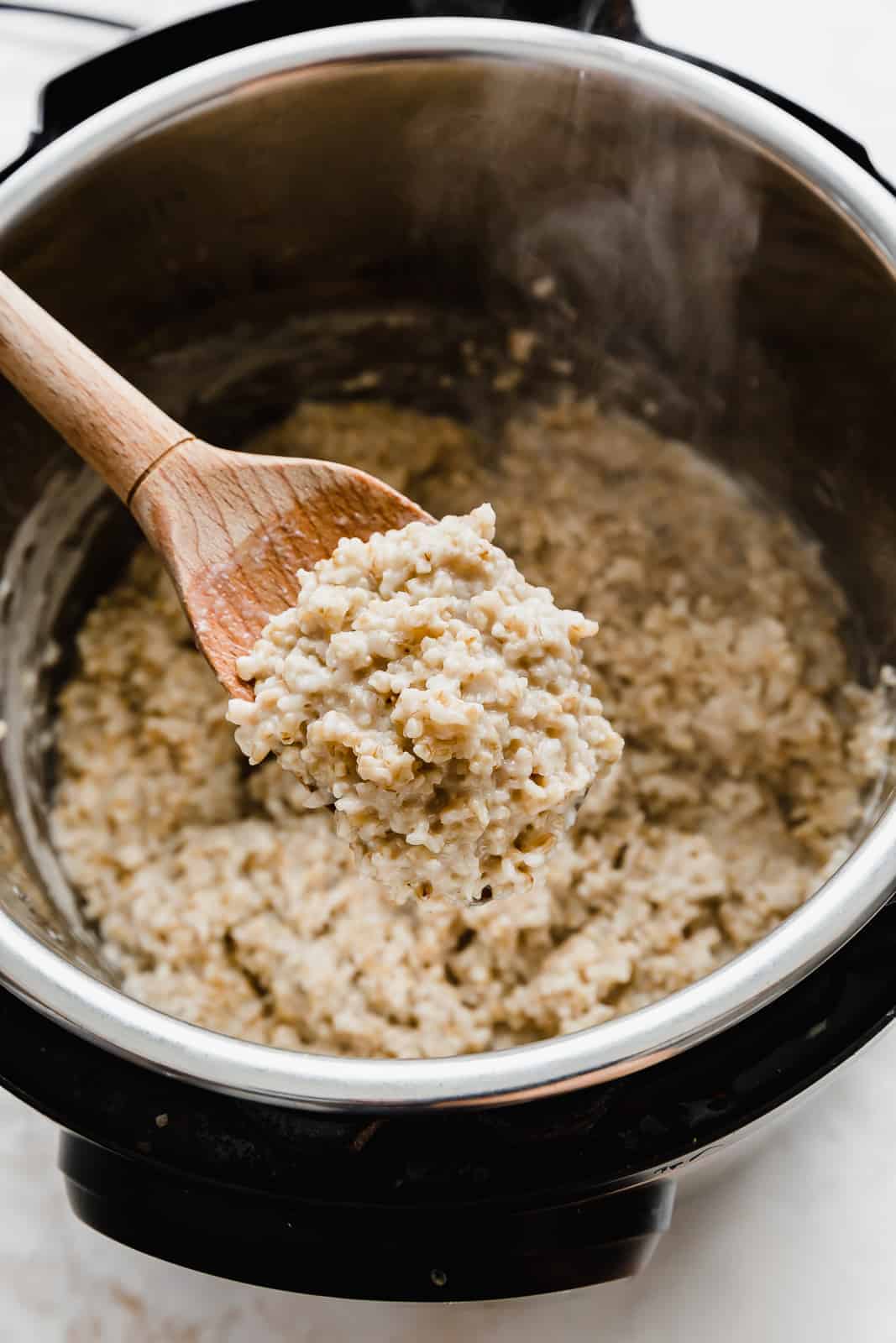 A wooden spoon holding up a scoop of creamy steel cut oats. 