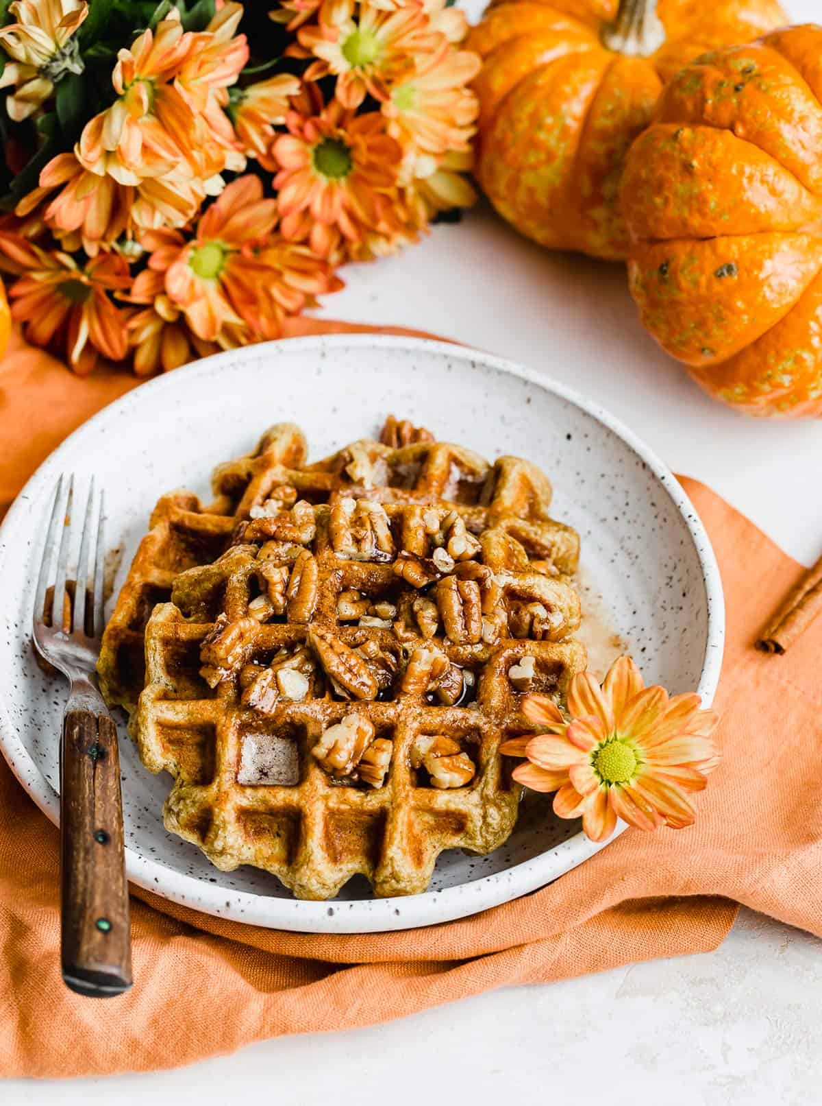 Two Pumpkin Waffles topped with pecans on a white plate.
