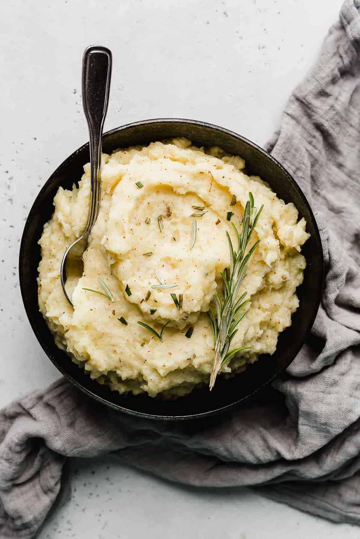 A black bowl filled with Rosemary Brown Butter Mashed Potatoes topped with a sprig of fresh rosemary.
