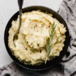 Rosemary Brown Butter Mashed Potatoes in a black bowl on a light gray background.