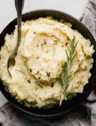 Rosemary Brown Butter Mashed Potatoes in a black bowl on a light gray background.