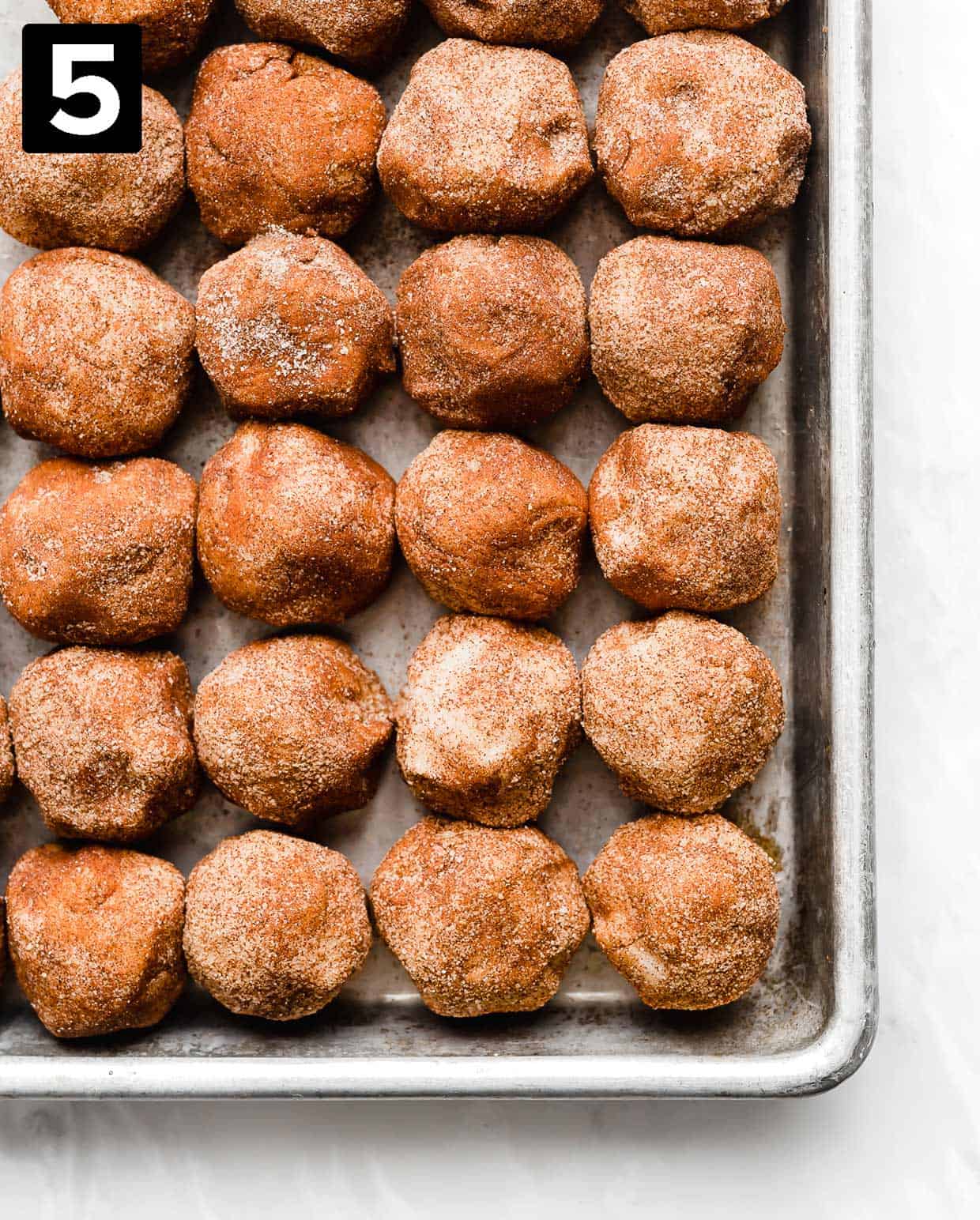 Cinnamon sugar coated snickerdoodle dough balls side by side on a baking sheet.