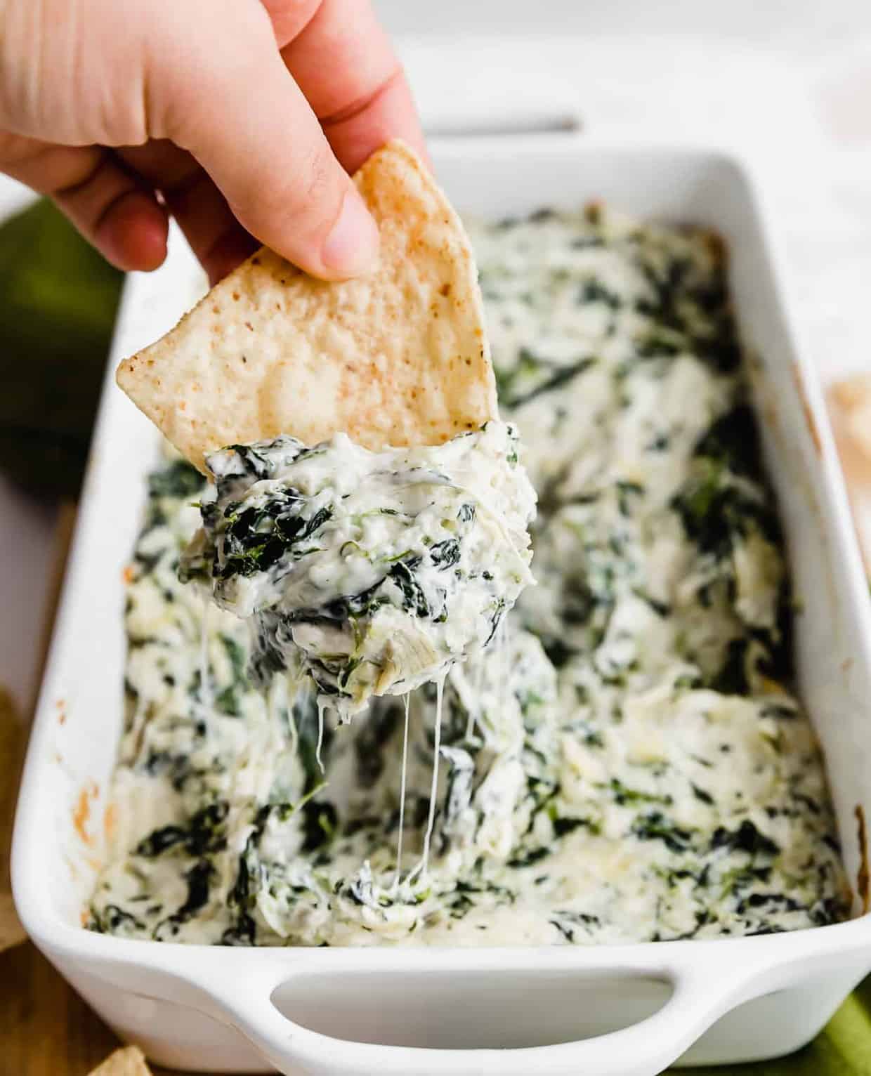 A tortilla chip dipping into Spinach Artichoke Dip.