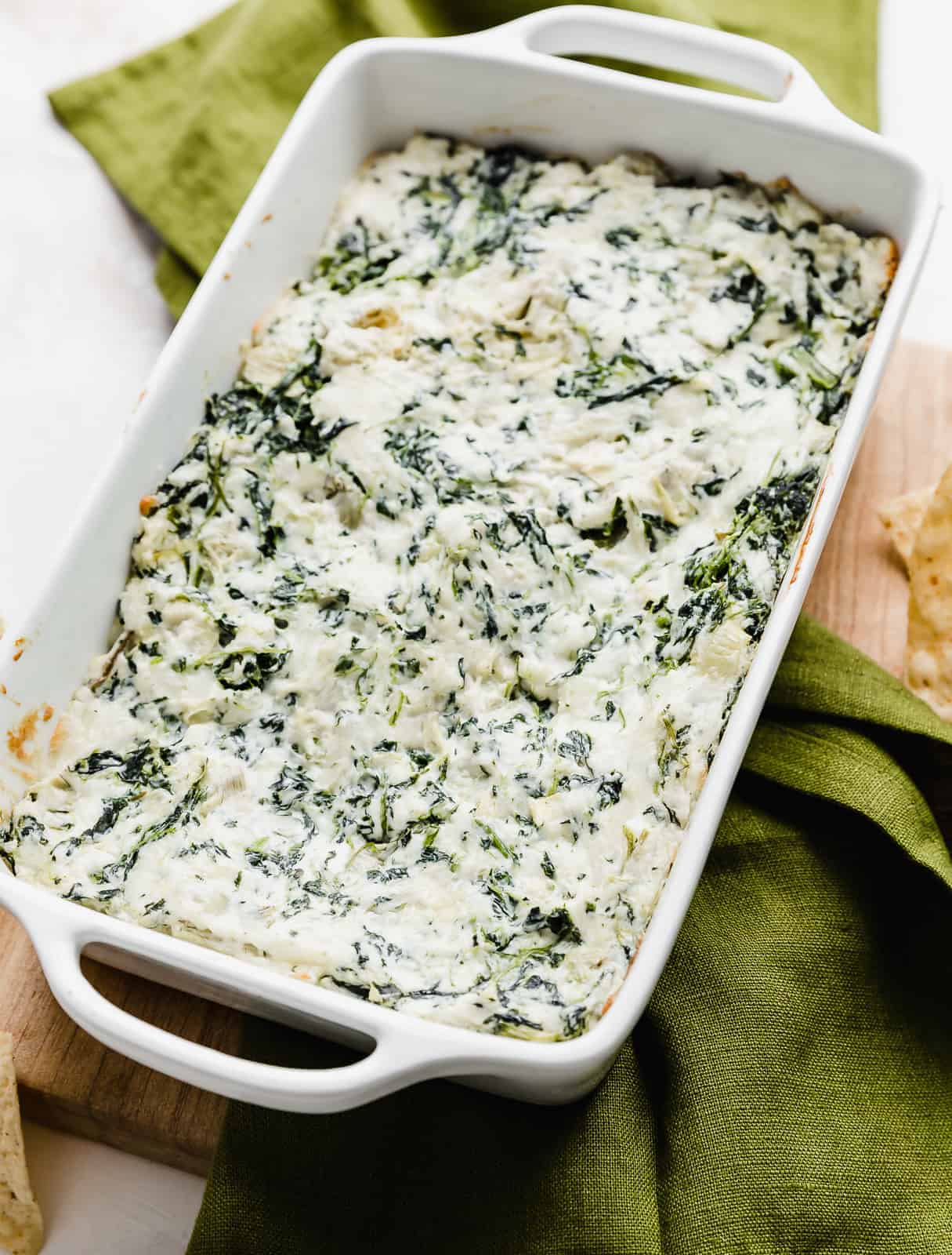 Spinach Artichoke Dip in a white baking dish resting on a dark green napkin.