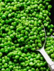 A silver serving spoon scooping up properly cooked frozen peas from a skillet.