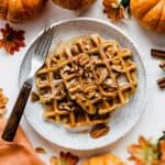 Two pumpkin waffles on a white plate, topped with pecans and syrup.