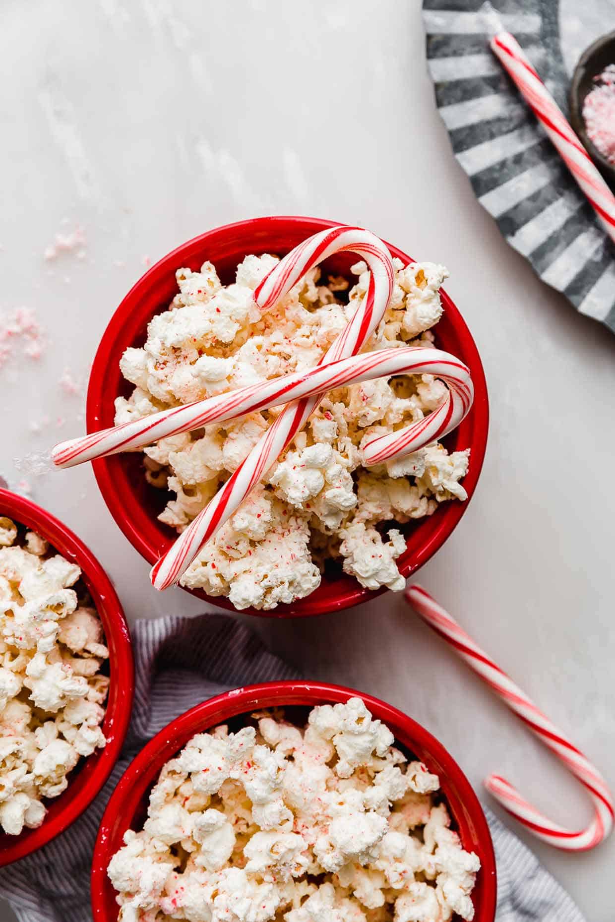 A red bowl filled with Candy Cane Popcorn and two candy canes on top.
