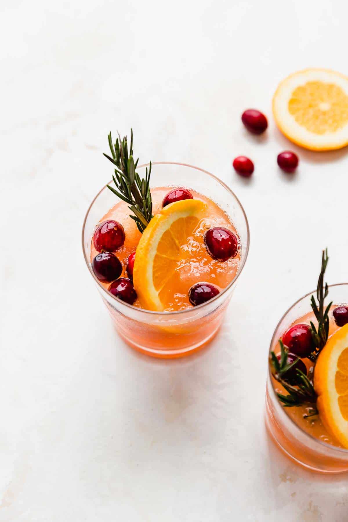 A cup of Christmas Punch on a white background, with fresh cranberries and an orange slice in each cup.