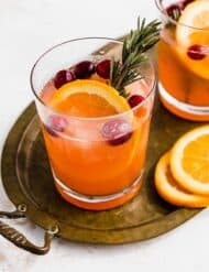 A clear glass filled with Christmas Slush Punch fresh cranberries and an orange slice.