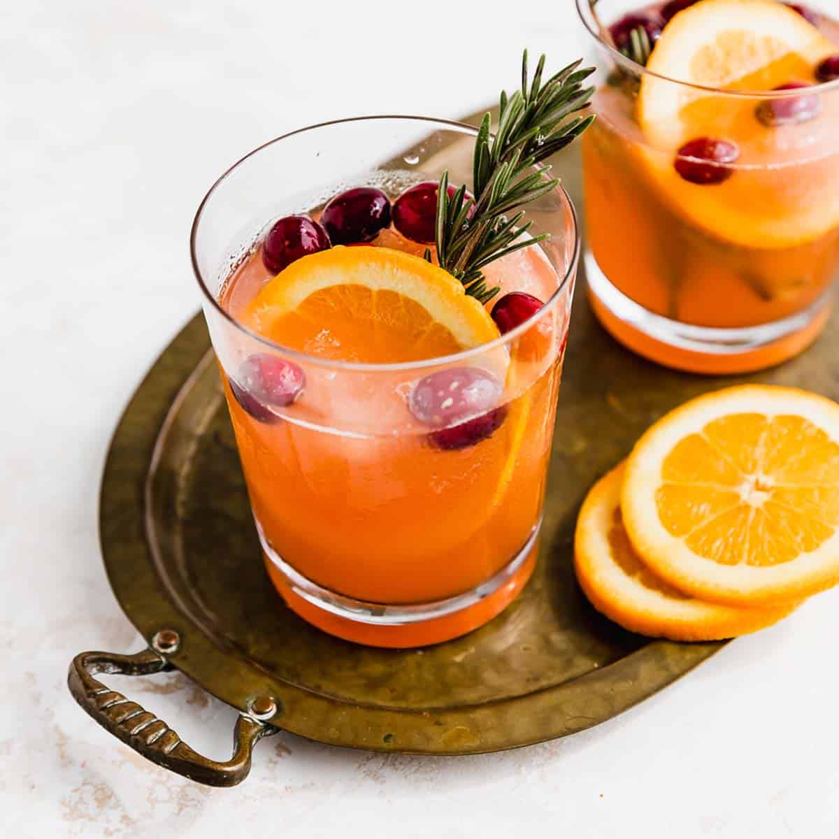 A clear glass filled with Christmas Slush Punch fresh cranberries and an orange slice.