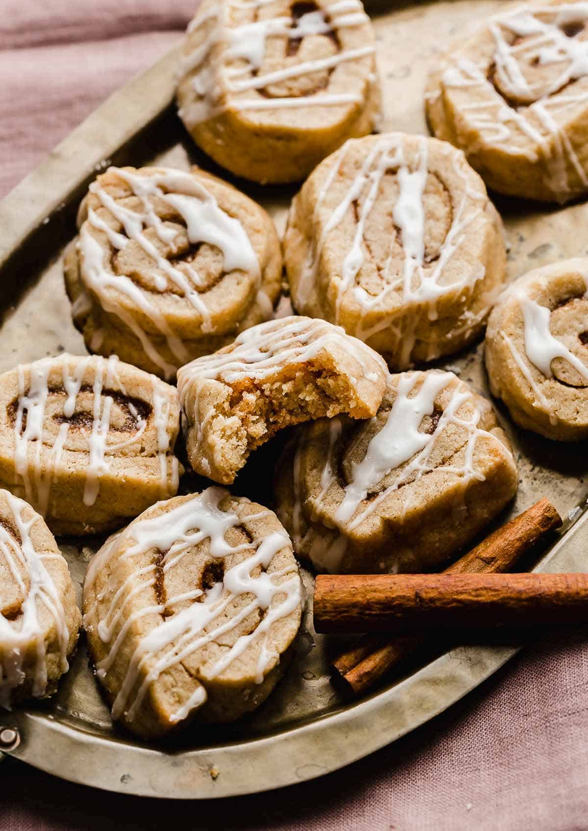 Glazed Cinnamon Roll Cookies on a bronze plate with one cookie having a bite taken out of it.