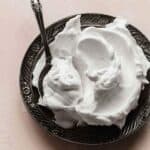 Coconut Whipped Cream on a black plate with a spoon scooped into the cream.