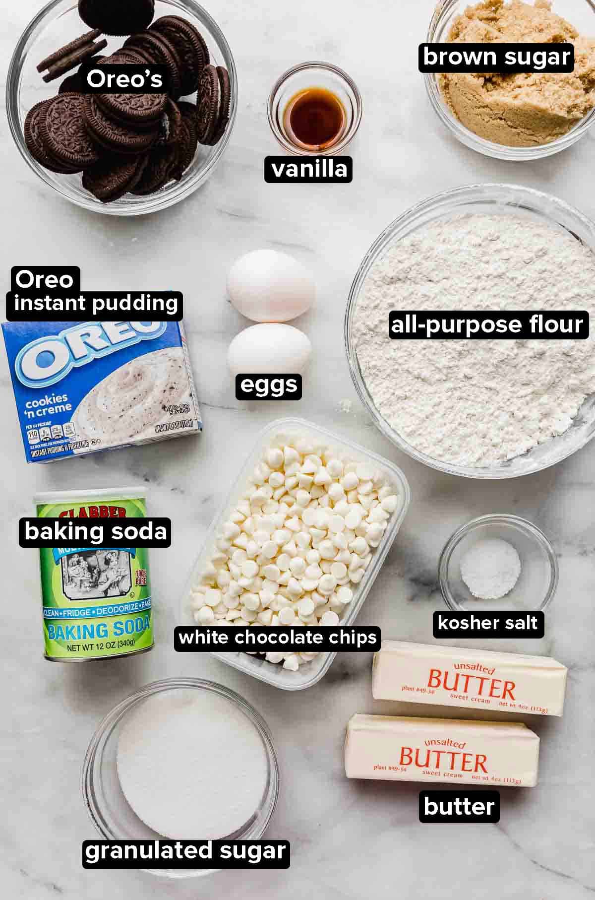 Cookies and Cream Cookies ingredients on a white background: Oreos, oreo pudding, flour, butter, white chocolate chips, eggs, sugar, and leavening agents.