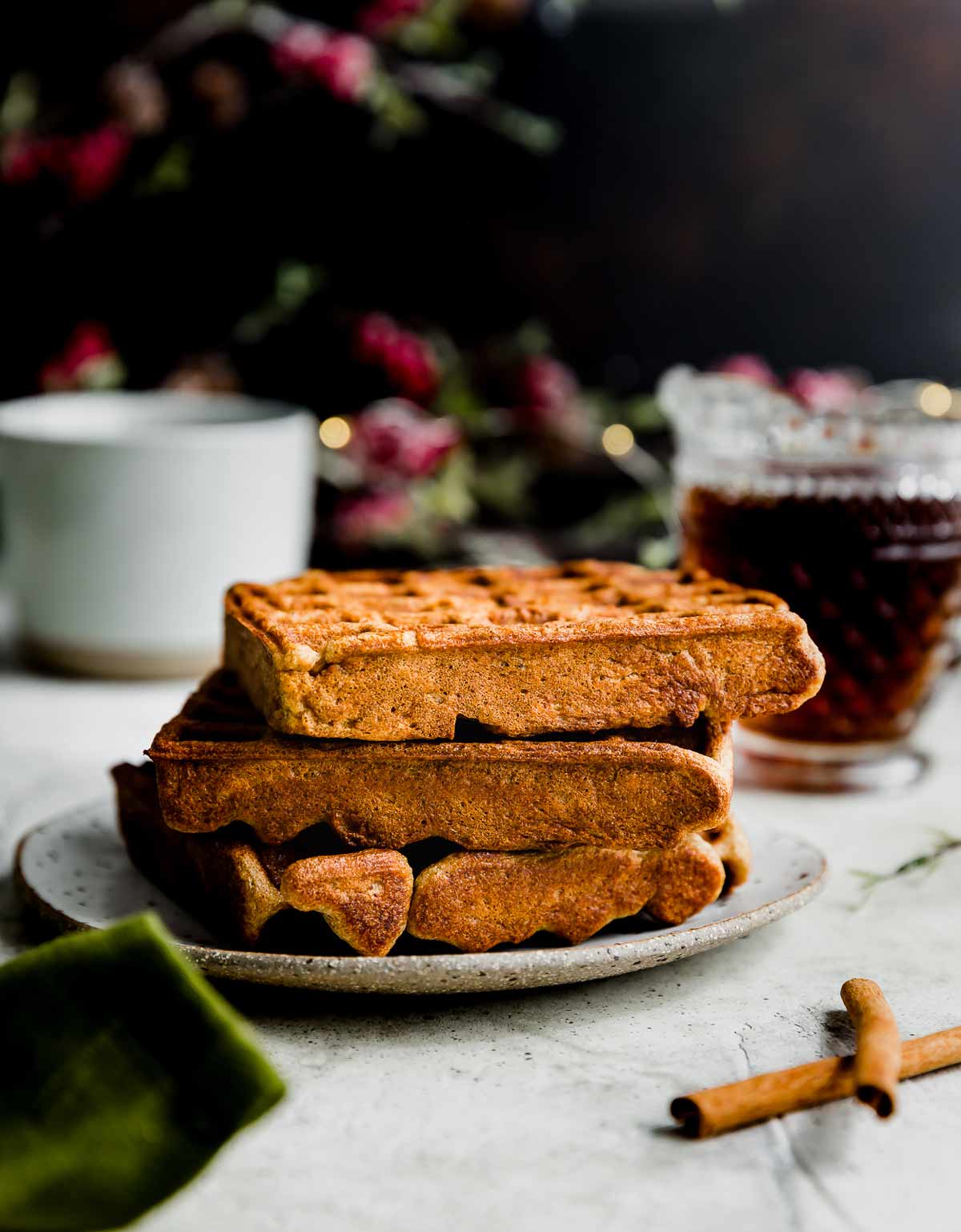 Square Gingerbread Waffles on a white plate with maple syrup in the background.