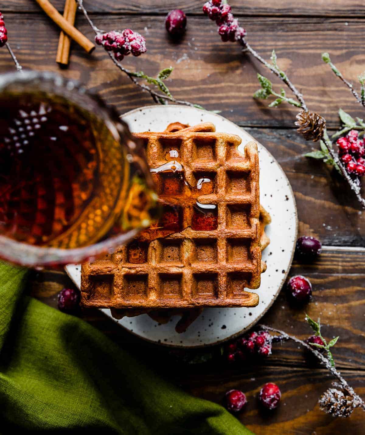 Maple syrup being poured overtop square Gingerbread Waffles.
