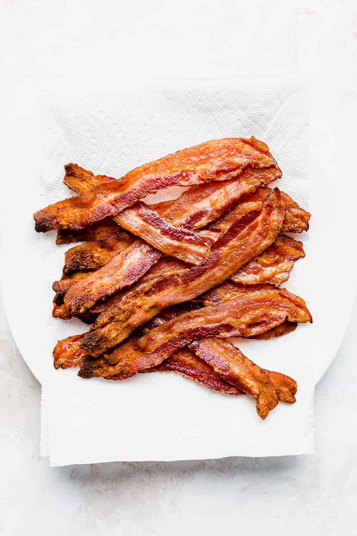 Crispy cooked bacon on a white paper towel lined plate.