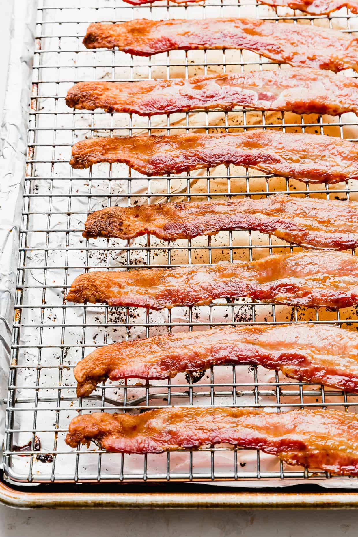 An angled shot of crispy bacon on a wire rack nested in a baking sheet. 