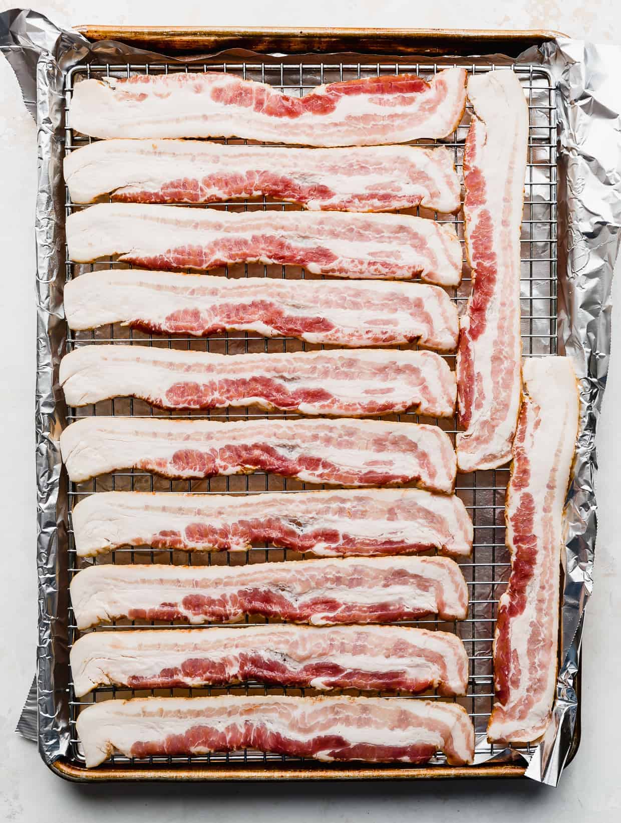 Raw bacon lined on a wire rack resting in a baking sheet. 