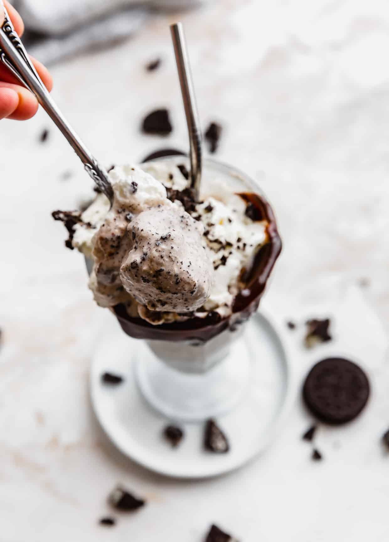 A spoon scooping out homemade Oreo milkshake from a glass cup.