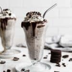 Two tall glasses full of Oreo milkshake topped with whipped cream and crushed Oreos.