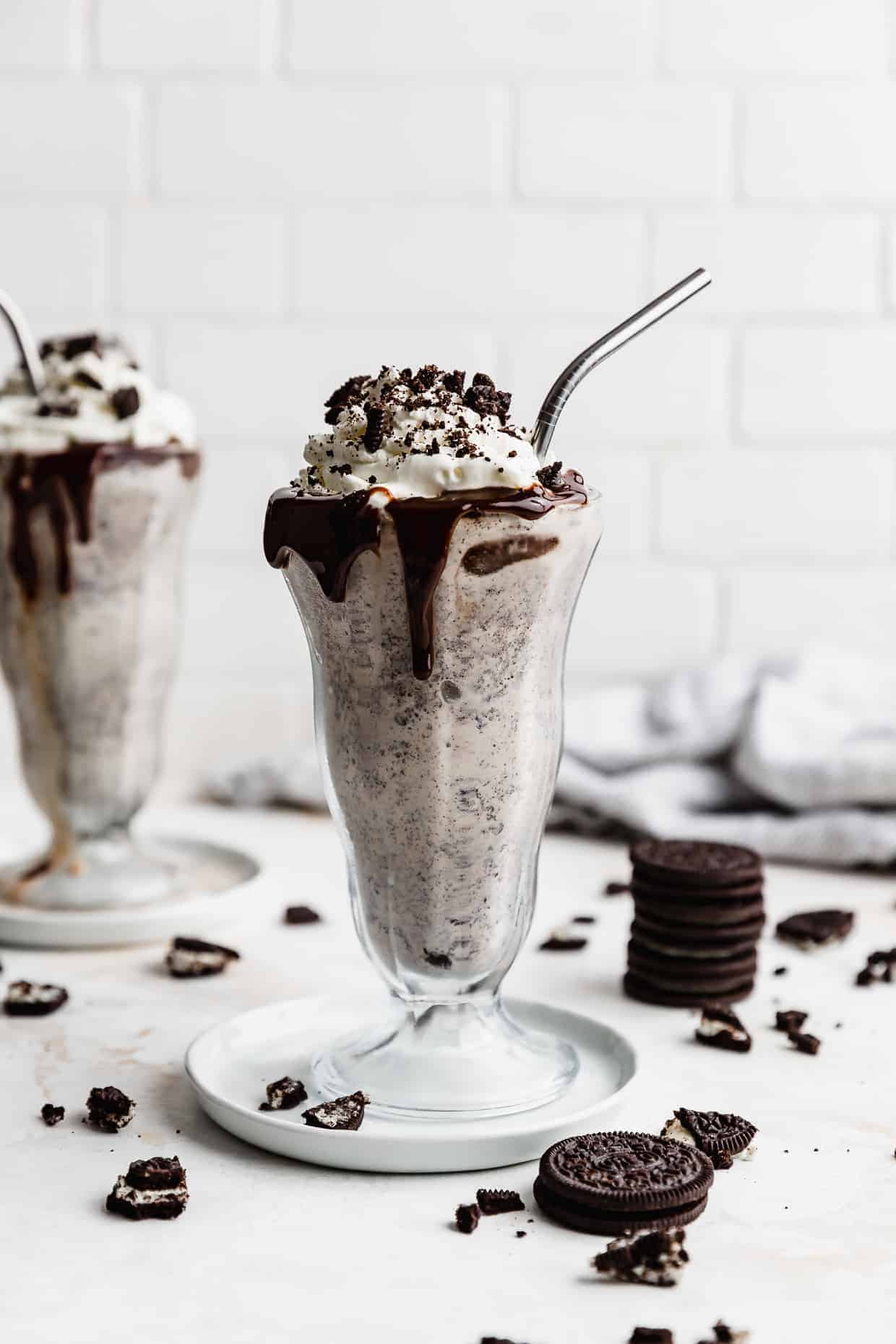 Two tall glasses full of Oreo milkshake topped with whipped cream and crushed Oreos. 