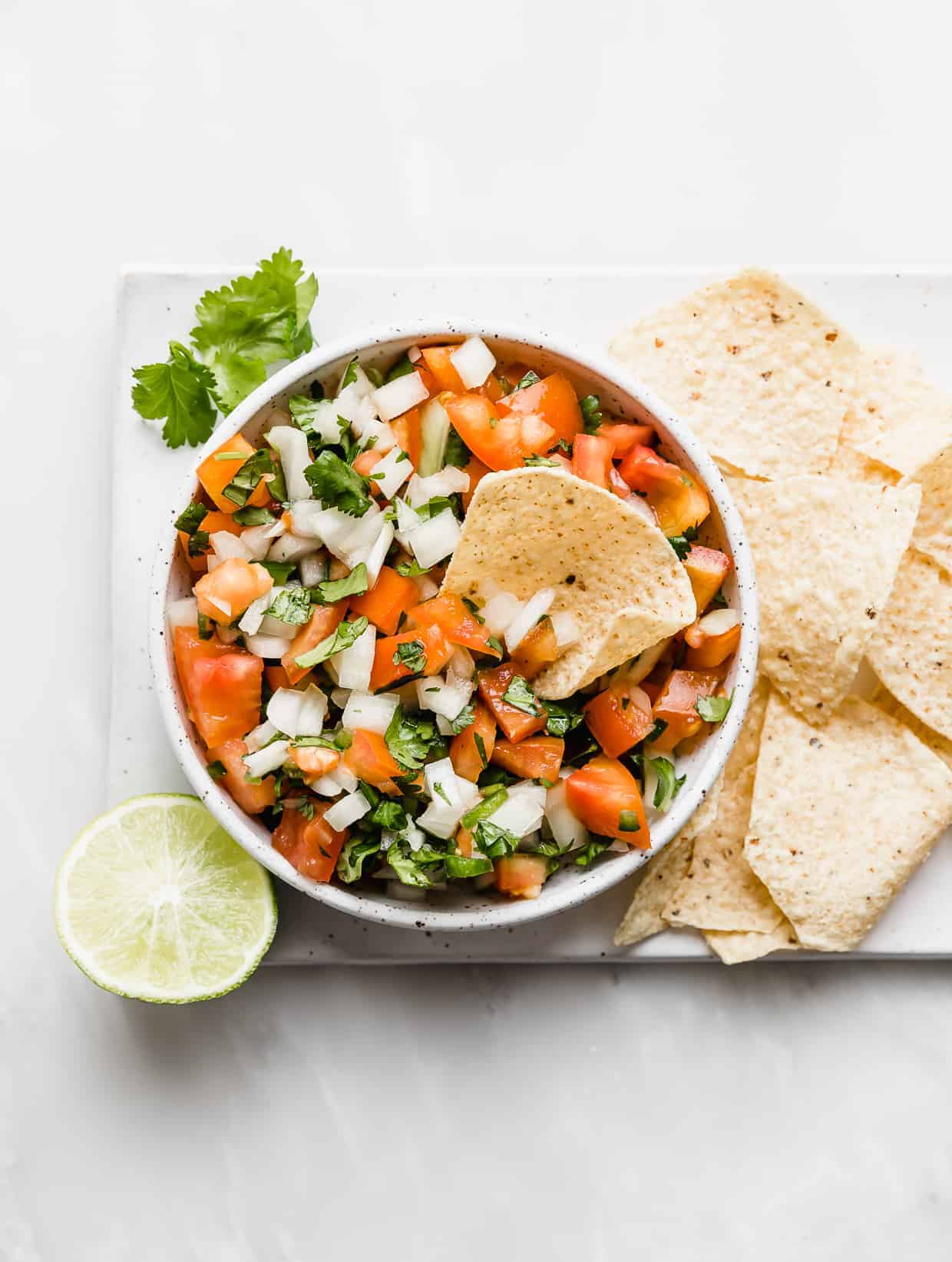 A bowl of fresh pico de Gallo with tortilla chips on the right side of the bowl. 