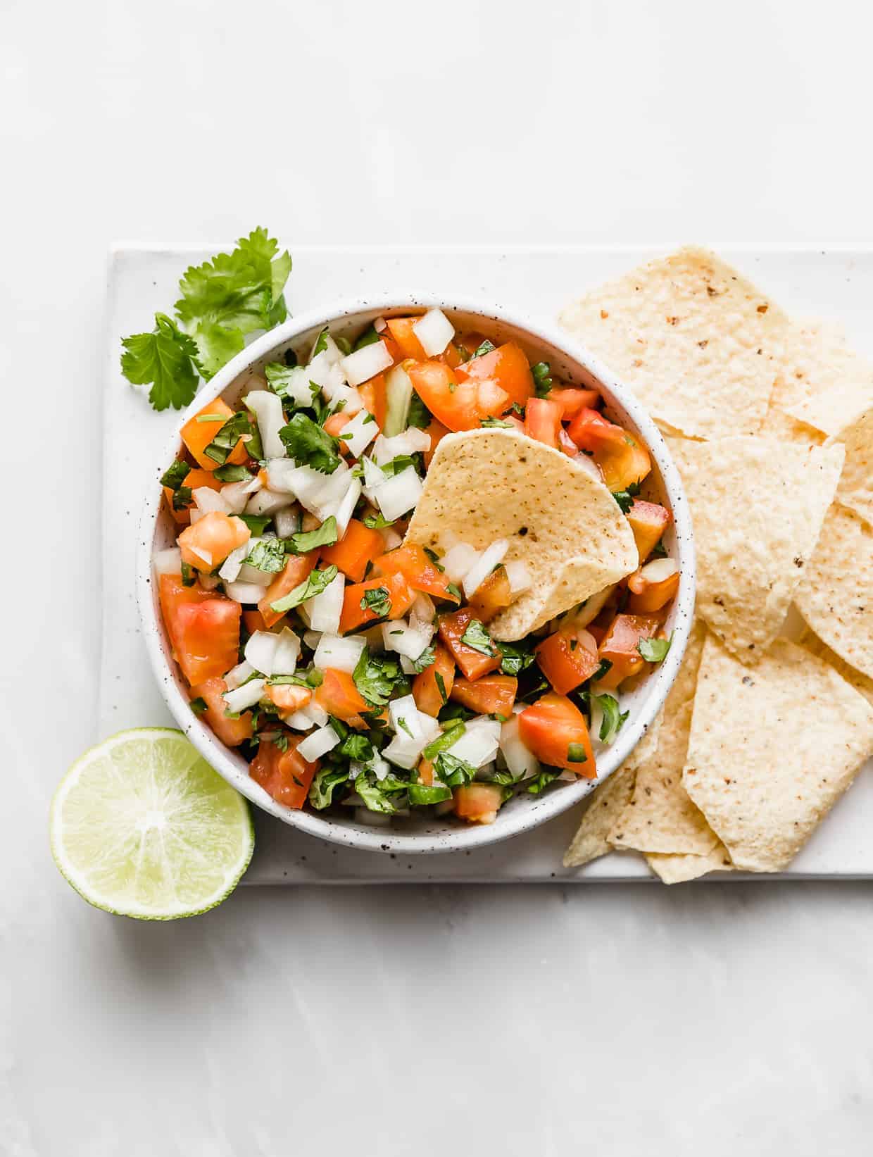 A bowl of fresh pico de Gallo with tortilla chips on the right side of the bowl.