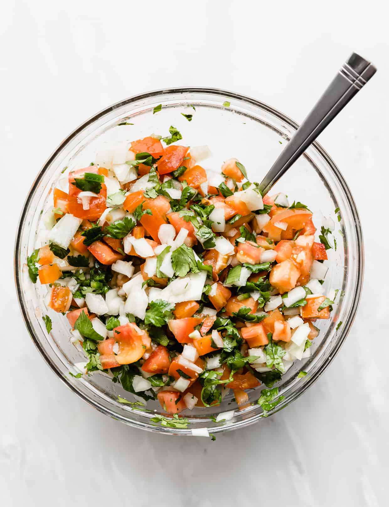 A glass bowl full of fresh Pico de Gallo against a white background.