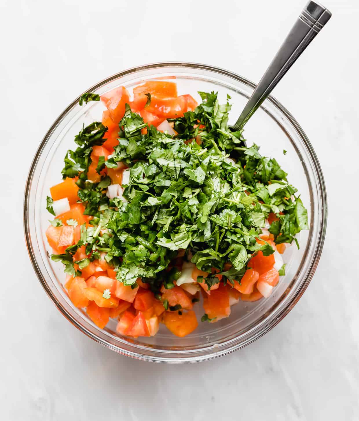 A glass bowl full of diced onion, tomato, and chopped cilantro. 