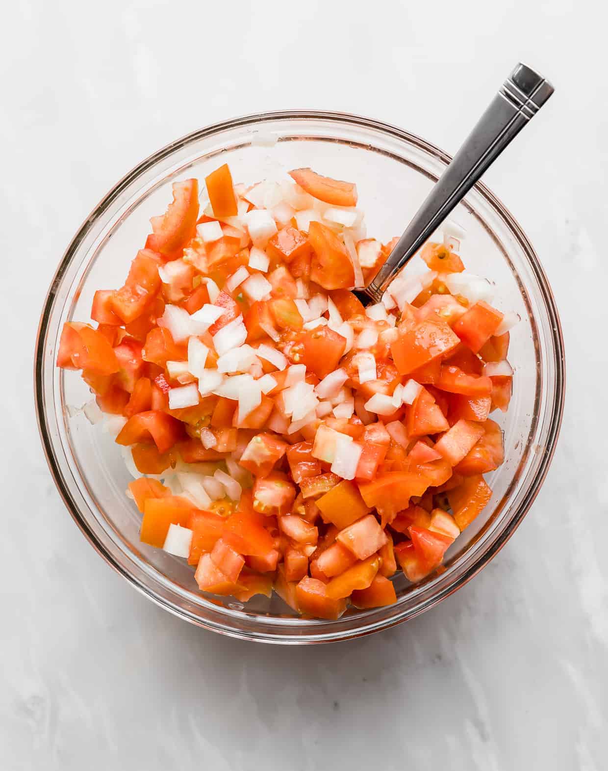 Diced onion and diced tomatoes in a glass bowl against a white background. 