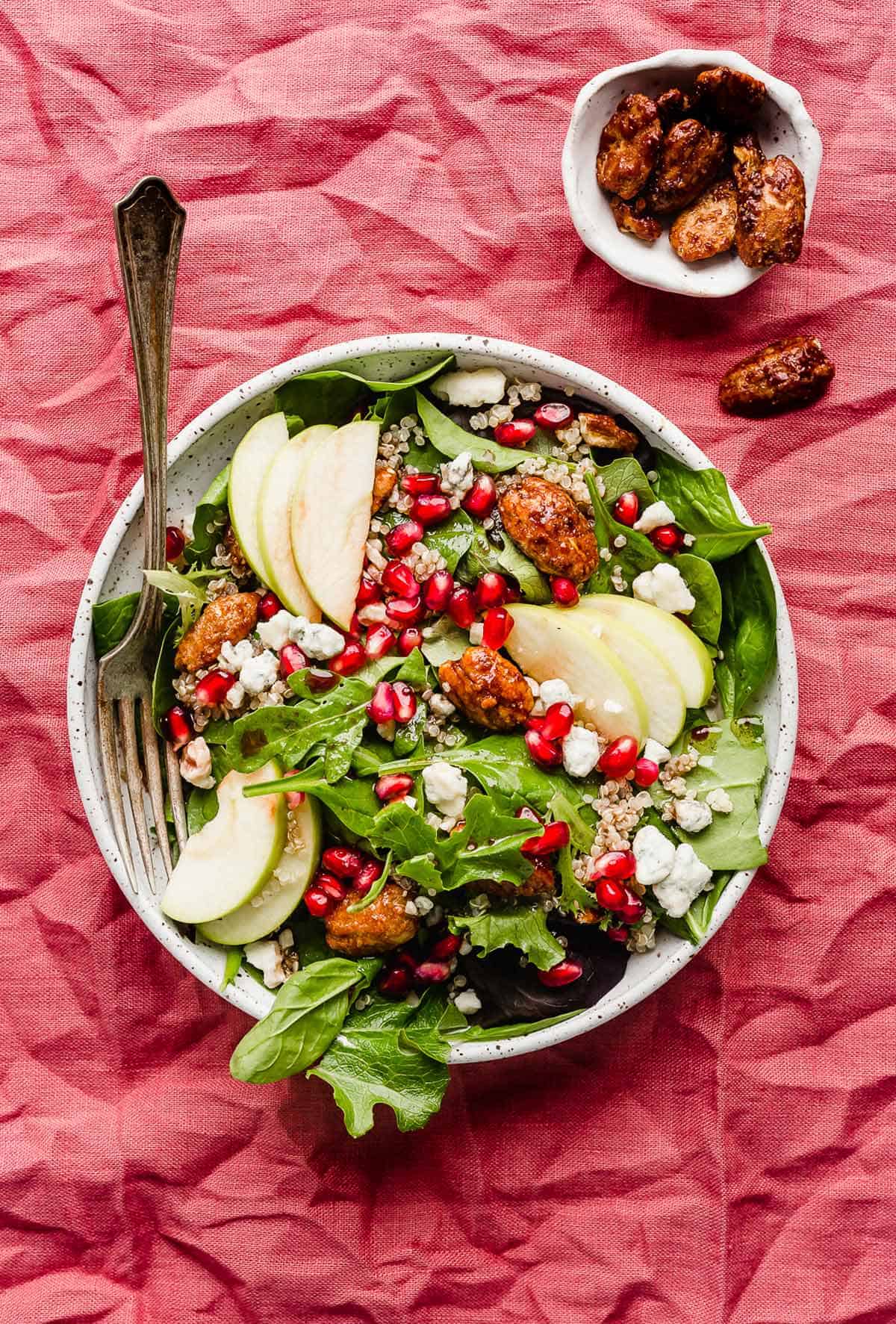 Pomegranate Salad on a white plate that's on a dark pink/red napkin.