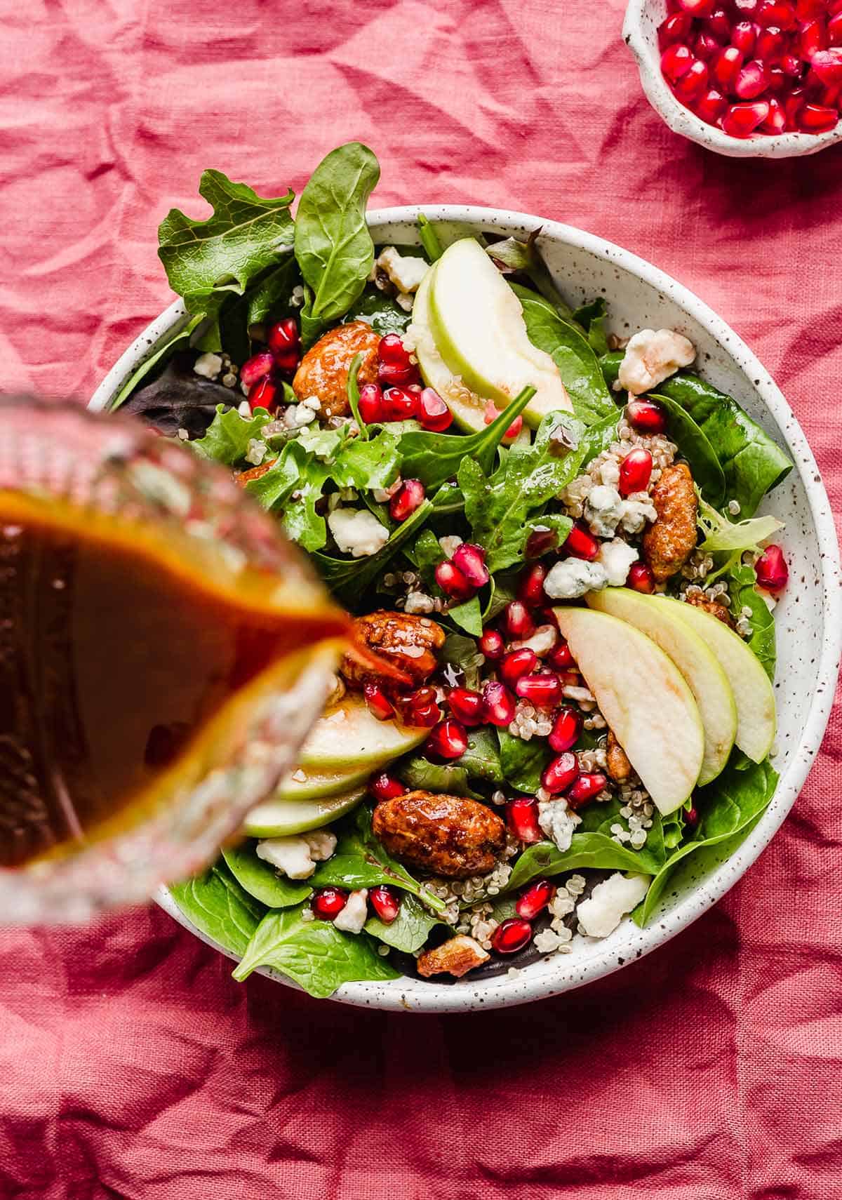 Pomegranate dressing being poured overtop a fresh Pomegranate Salad.