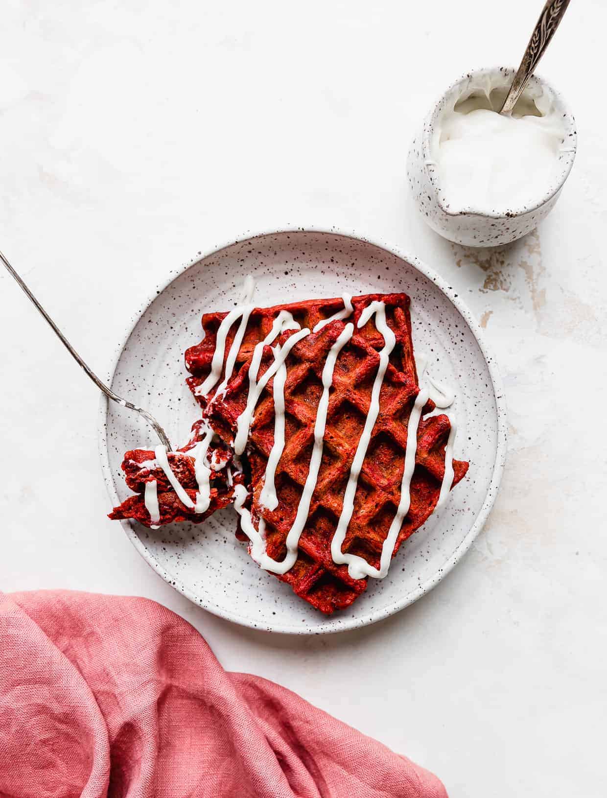 Red velvet waffles drizzled in a white cream cheese glaze against a white background.