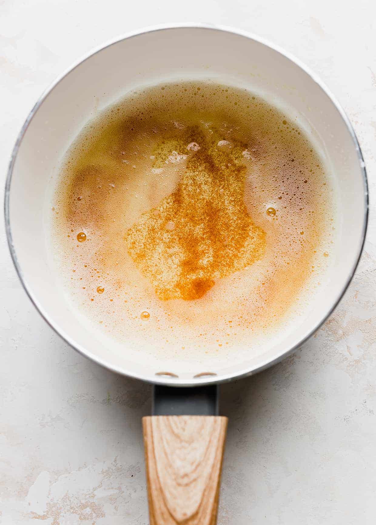 A white sauce pan with browned butter (a light amber color) in it.