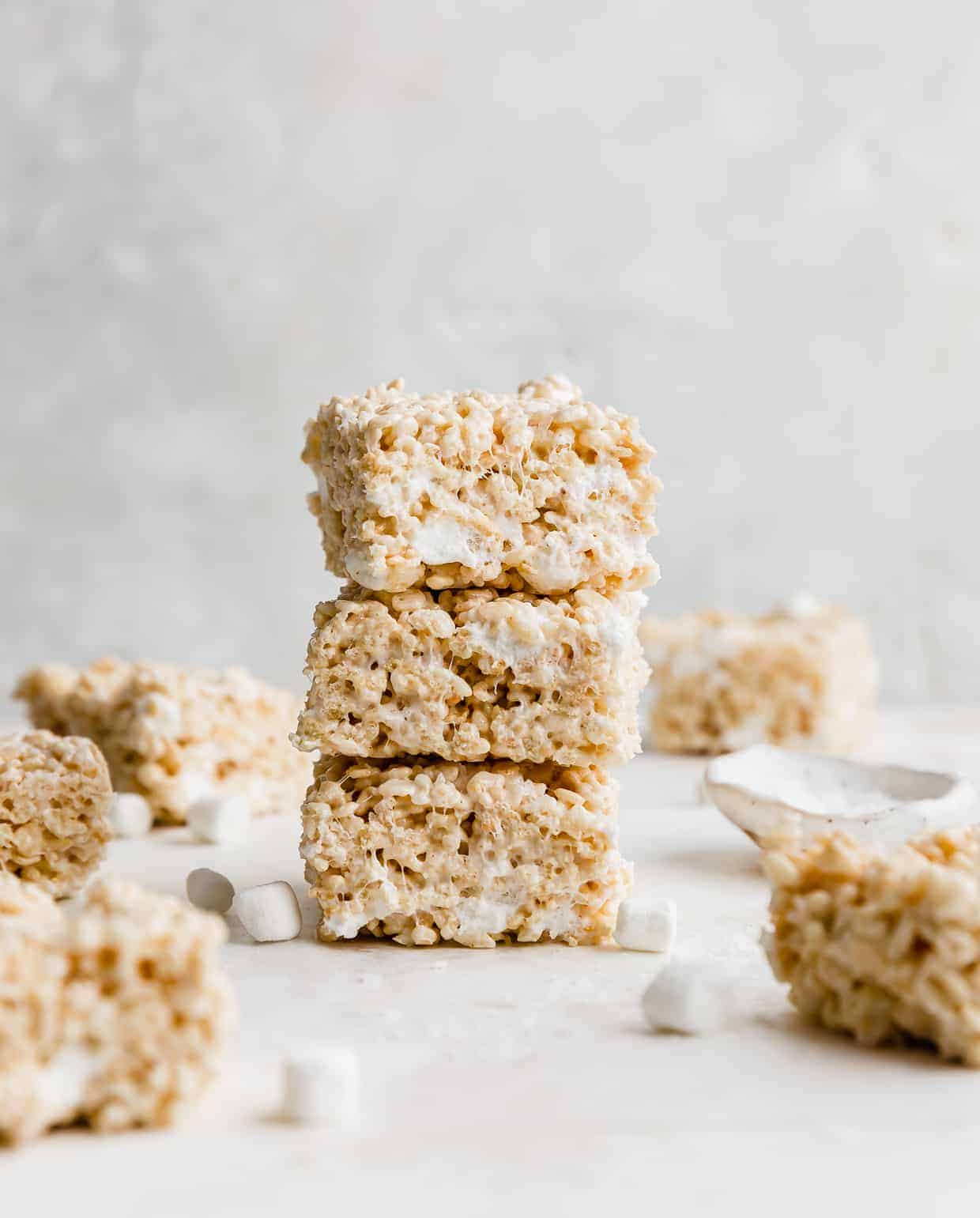 Three, thick, brown butter Rice Krispie treats stacked on top of each other, with mini marshmallows scattered around the base.