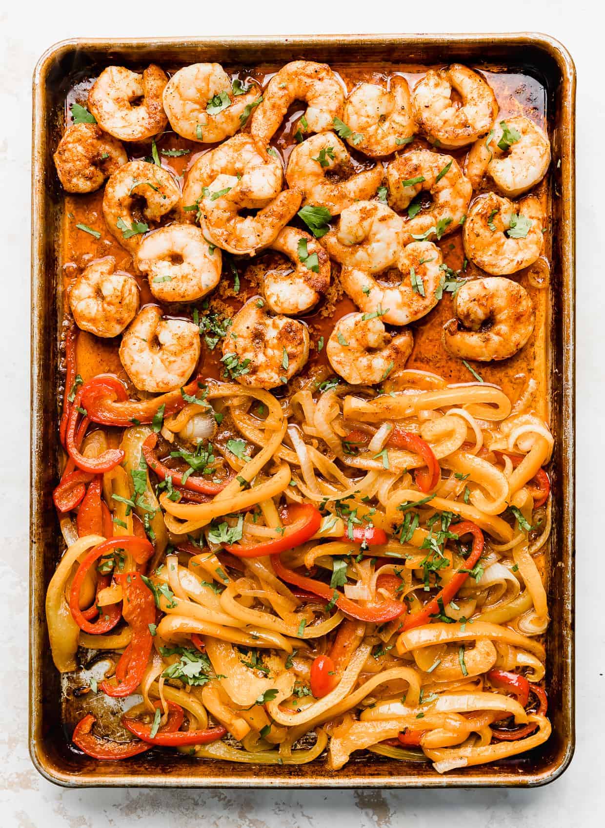 Cooked shrimp and sliced peppers on a baking sheet topped with chopped cilantro.