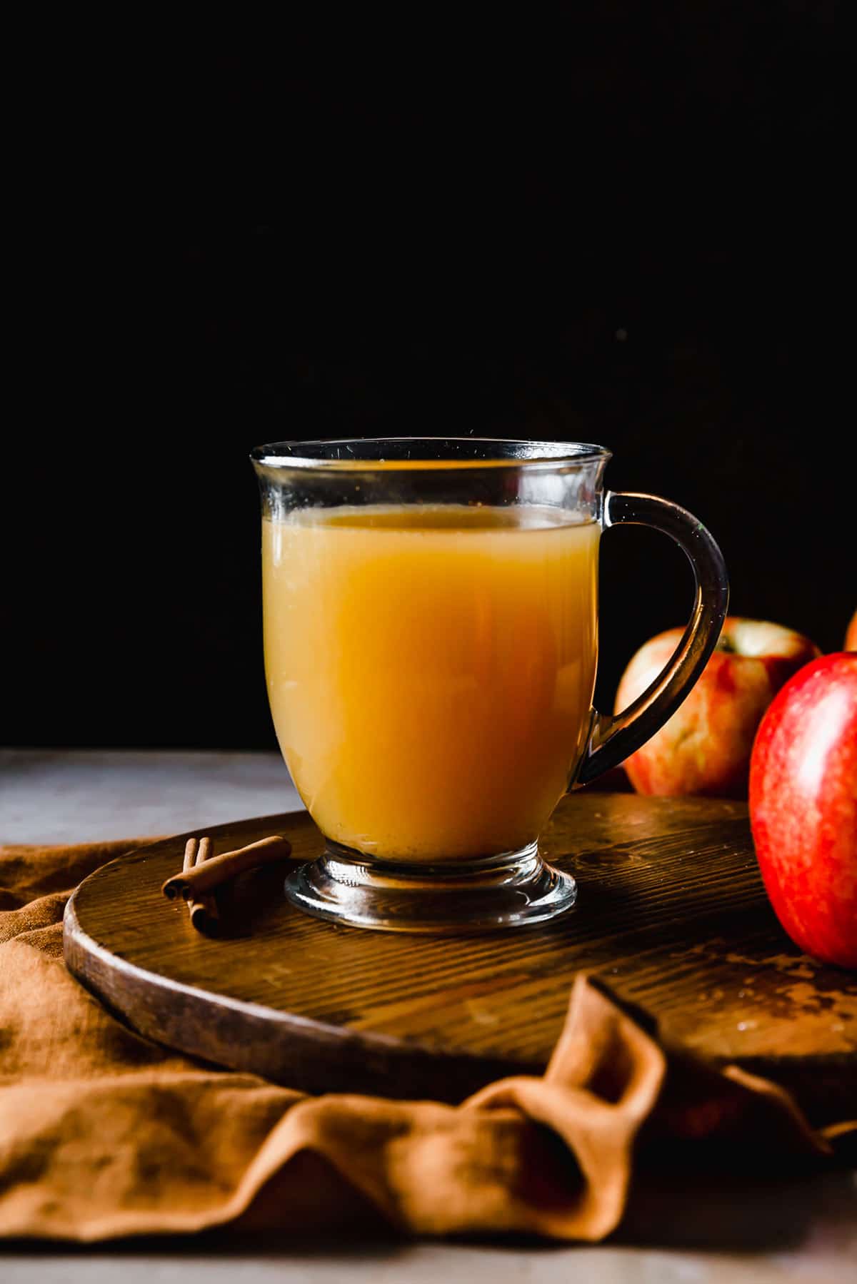 A clear mug filled with Hot Wassail against a black background.