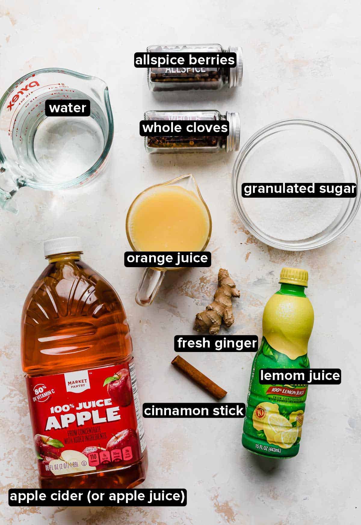 Homemade wassail ingredients on a white textured background: apple cider or apple juice, orange juice, lemon juice, water, sugar, and spices.