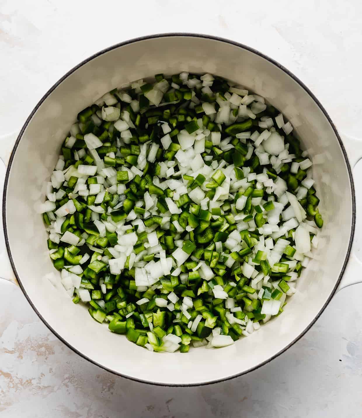 A white pot full of diced onion and diced green peppers.