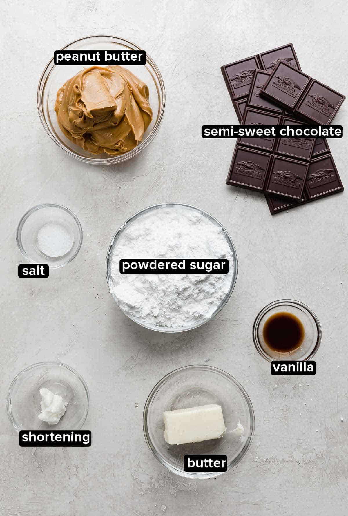 Buckeyes recipe ingredients portioned into glass bowls on a gray background: butter, vanilla, shortening, powdered sugar, salt, peanut butter, and chocolate.