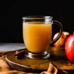 Hot Wassail recipe in a clear mug with apples next to the right of the mug.
